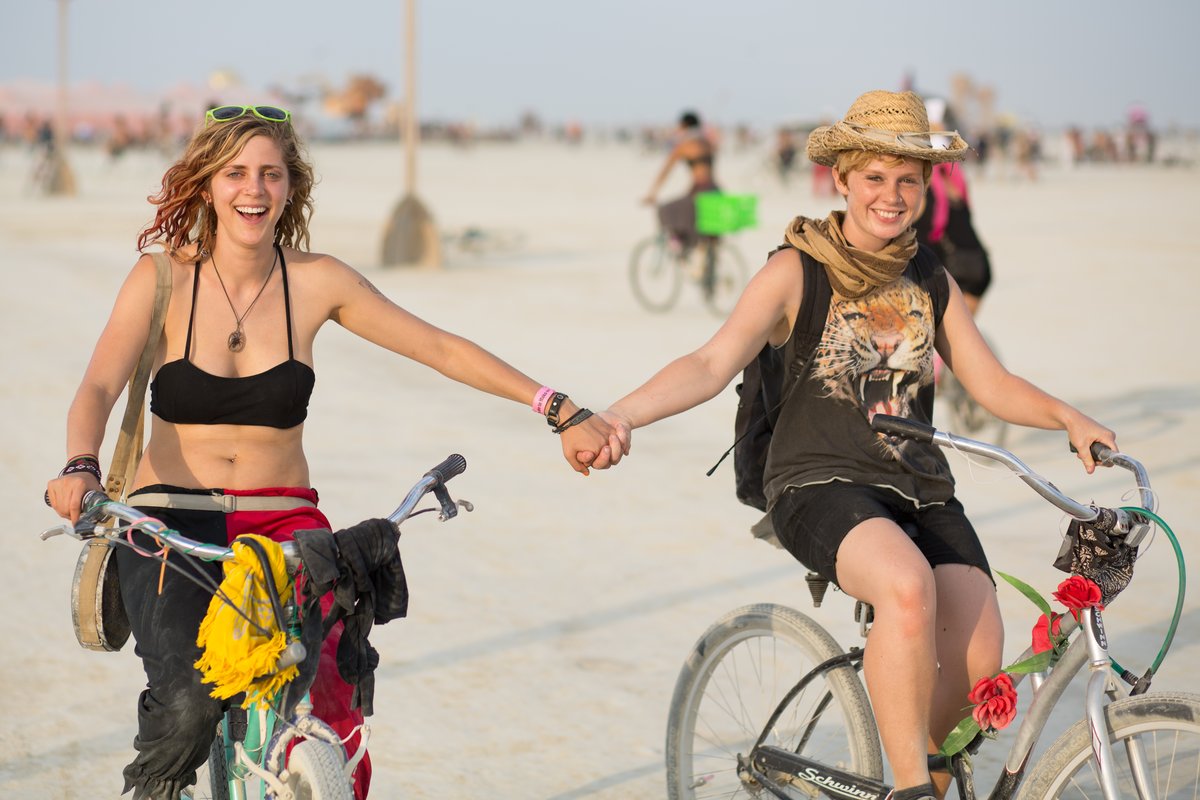 Two Happy Burners Hold Hands While Riding Bikes