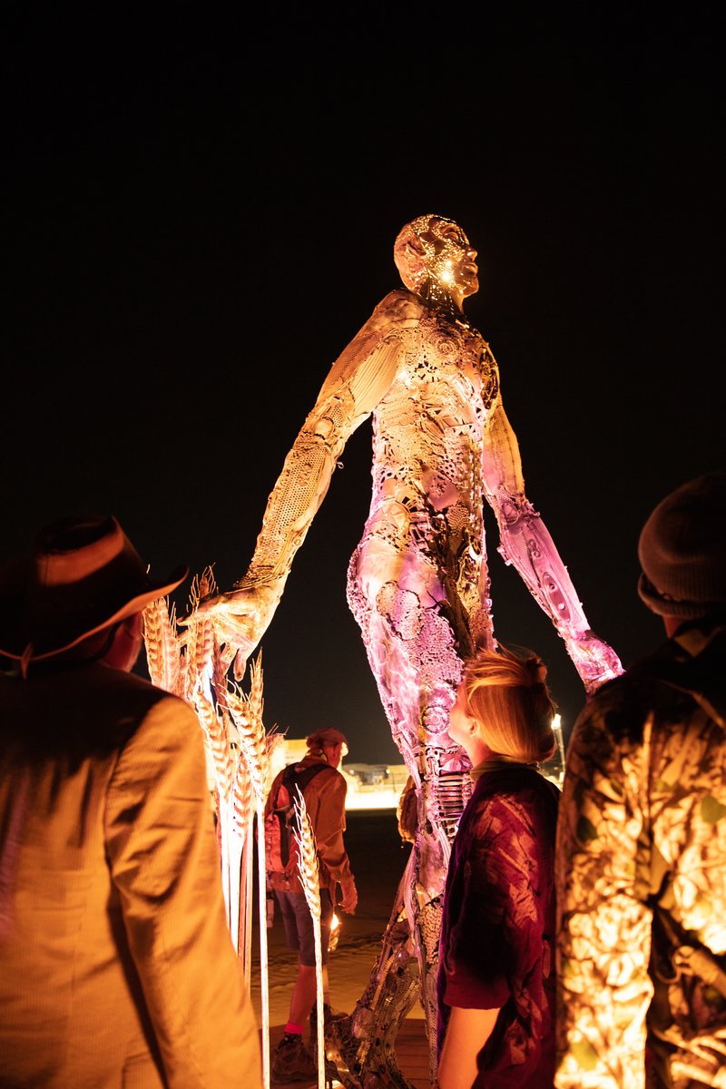 Passage by: Dana Albany from: San Francisco, CA year: 2018 Passage is an installation of a man, in a captive gesture, leisurely walking while its hand sweeps through stalks of wheat. The sculpture clearly highlights characteristics of a human form; muscle, sinuous tendon, sculpted hands, feet. Yet, it's a composite of mechanical debris and steel. Viewers may hypothesize, is this a man? is it part robot? and what is the blurry fine-line between each? The other huge component is the presence of the wheat. It symbolizes abundance, life, fertility. It is food, subsistence, of which without, the human race would be extinct. Viewers can look closer at the inherent beauty of the human form, contemplate mechanics/technology or most importantly, be reminded of our absolute reliance on nature in the end.