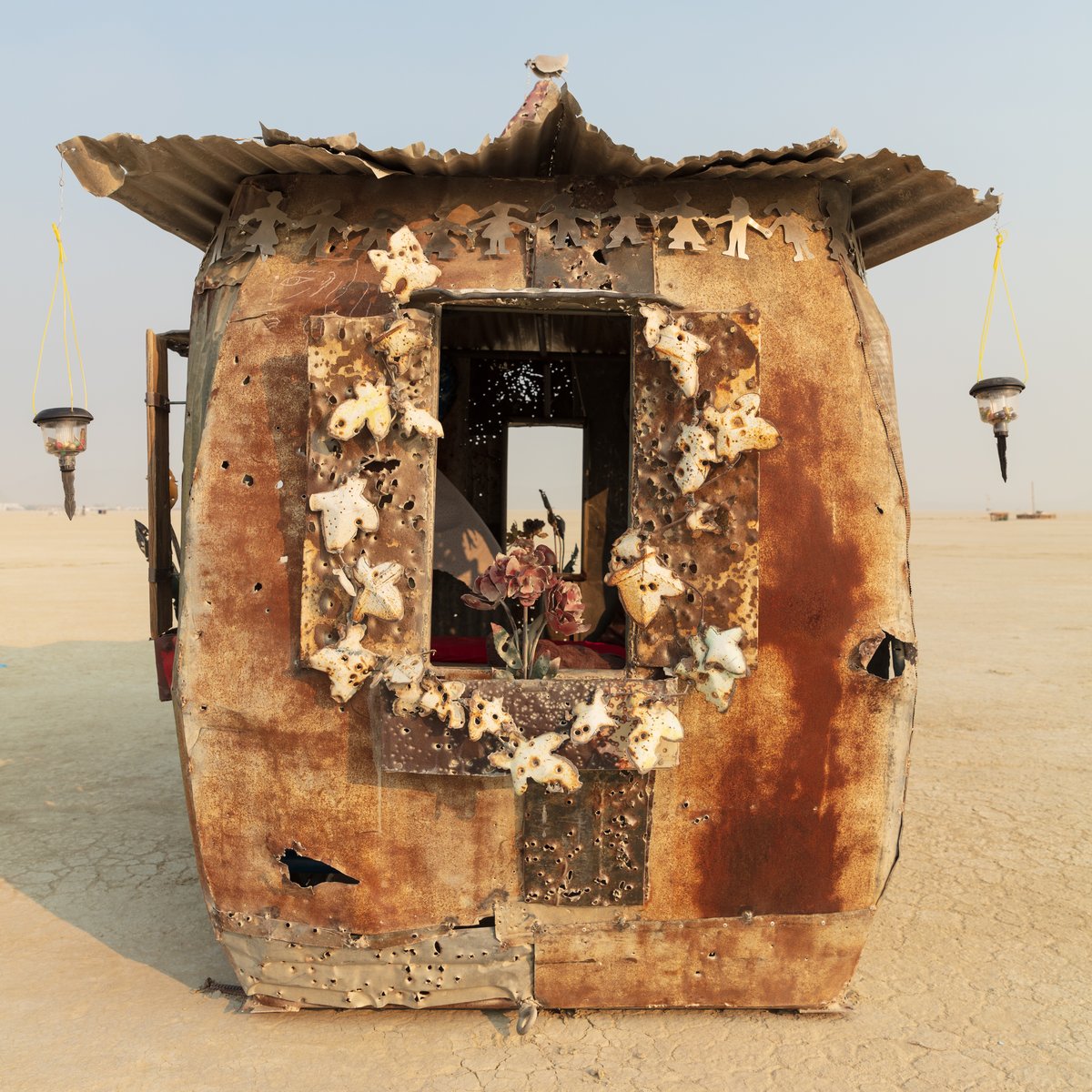 The Little Schoolhouse of Hope and Fear by: Gratis from: Vista, CA year: 2018 If all you had was the rough detritus of war, the cheap rubble of constant calamity, what would you build with it? A bunker, a church, or a school? Would you create a place of hope or fear? Of the past or for the future? Hope rising up from a violent and chaotic past, Fear transformed into building blocks: found metal, often riddled by gunre, torn by the wind and baked by the desert sun are incorporated into this replica of the traditional "little red schoolhouse." The Little Schoolhouse of Hope and Fear stands on the playa as a beacon to those who wish to teach a better way for the future, or to those ready to learn from the failures of the past.