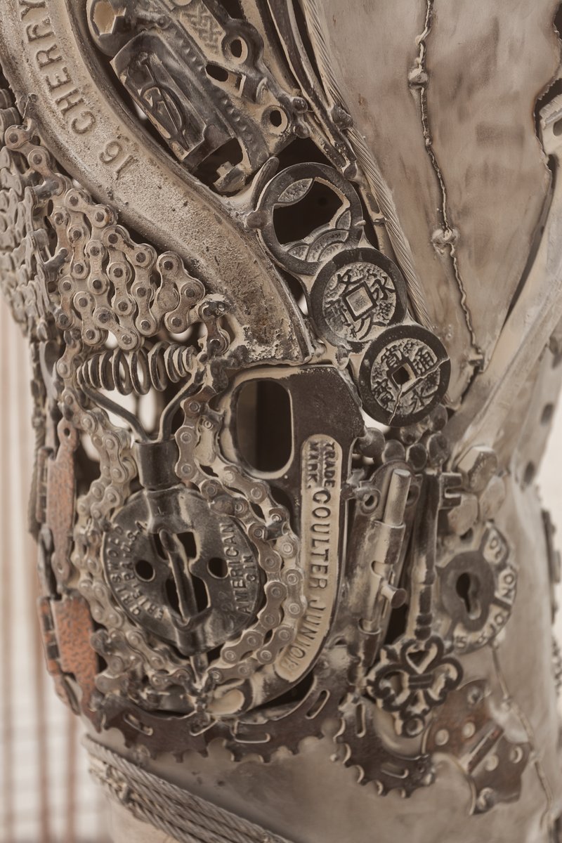 Passage by: Dana Albany from: San Francisco, CA year: 2018 Passage is an installation of a man, in a captive gesture, leisurely walking while its hand sweeps through stalks of wheat. The sculpture clearly highlights characteristics of a human form; muscle, sinuous tendon, sculpted hands, feet. Yet, it's a composite of mechanical debris and steel. Viewers may hypothesize, is this a man? is it part robot? and what is the blurry fine-line between each? The other huge component is the presence of the wheat. It symbolizes abundance, life, fertility. It is food, subsistence, of which without, the human race would be extinct. Viewers can look closer at the inherent beauty of the human form, contemplate mechanics/technology or most importantly, be reminded of our absolute reliance on nature in the end.