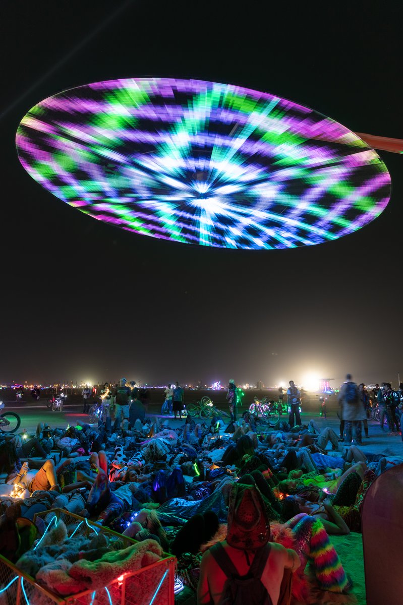 Paraluna by: Christopher Schardt from: Oakland, CA year: 2018 Paraluna combines kinetic sculpture, LEDs and music. Its main component is a disc 10m in diameter with 17,280 LEDs. A computer controls the LEDs while rotating, raising, lowering, and tilting the disc. Some of the LED patterns work with the rotation of the disk, creating spirals. Others use persistence-of-vision, making an image hover in space above the spinning LEDs. Spokes demonstrates both of these styles: https://photos.app.goo.gl/DcP9IauNTjRHENUh2 Surrounding the disc are several high-quality speakers that play classical music at comfortable, yet immersive volume, creating a comfortable, peaceful place to be. Patterns are chosen to complement each musical piece, as with Firmament: https://photos.app.goo.gl/H6KCzkf5jkGWAA3m2