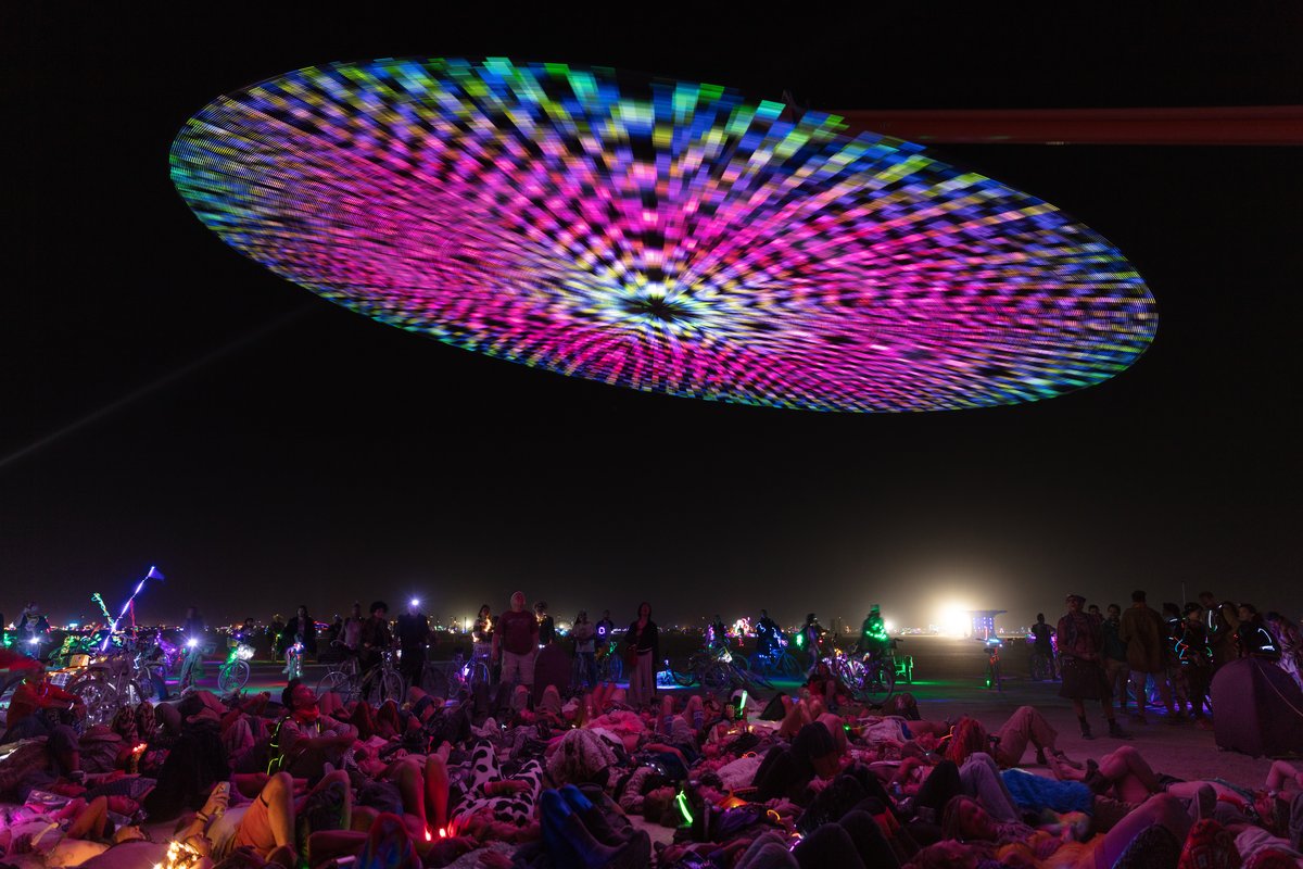 Paraluna by: Christopher Schardt from: Oakland, CA year: 2018 Paraluna combines kinetic sculpture, LEDs and music. Its main component is a disc 10m in diameter with 17,280 LEDs. A computer controls the LEDs while rotating, raising, lowering, and tilting the disc. Some of the LED patterns work with the rotation of the disk, creating spirals. Others use persistence-of-vision, making an image hover in space above the spinning LEDs. Spokes demonstrates both of these styles: https://photos.app.goo.gl/DcP9IauNTjRHENUh2 Surrounding the disc are several high-quality speakers that play classical music at comfortable, yet immersive volume, creating a comfortable, peaceful place to be. Patterns are chosen to complement each musical piece, as with Firmament: https://photos.app.goo.gl/H6KCzkf5jkGWAA3m2