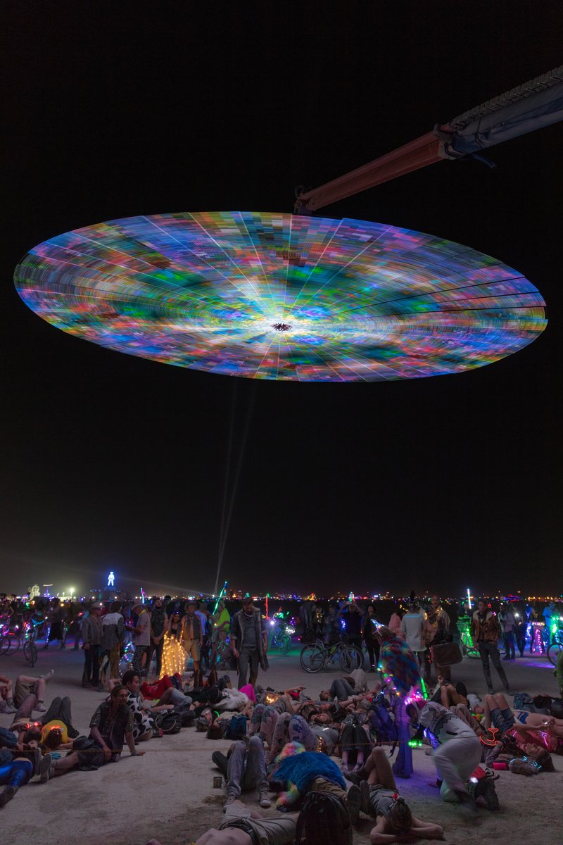 Paraluna by: Christopher Schardt from: Oakland, CA year: 2018 Paraluna combines kinetic sculpture, LEDs and music. Its main component is a disc 10m in diameter with 17,280 LEDs. A computer controls the LEDs while rotating, raising, lowering, and tilting the disc. Some of the LED patterns work with the rotation of the disk, creating spirals. Others use persistence-of-vision, making an image hover in space above the spinning LEDs. Spokes demonstrates both of these styles: https://photos.app.goo.gl/DcP9IauNTjRHENUh2 Surrounding the disc are several high-quality speakers that play classical music at comfortable, yet immersive volume, creating a comfortable, peaceful place to be. Patterns are chosen to complement each musical piece, as with Firmament: https://photos.app.goo.gl/H6KCzkf5jkGWAA3m2