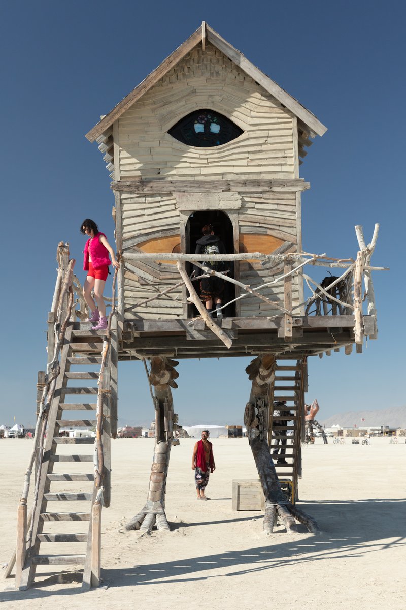 Baba Yaga's House by: Jessi Sprocket Janusee and Baba Yaga's Book Club from: Reno, NV year: 2018 The house of Baba Yaga will rise from the playa straddling it's mechanical chicken legs. The crone's house will be poised to run at the slightest provocation. Ascend her staircases to test the old witch if you dare. Are you able to walk through the veil of mortality into the space where the seer dwells? If you are strong of will, feeling bold and willing to show vulnerability she may allow you to venture within her sanctum. URL: http://jessisprocket.com/baba-yaga/