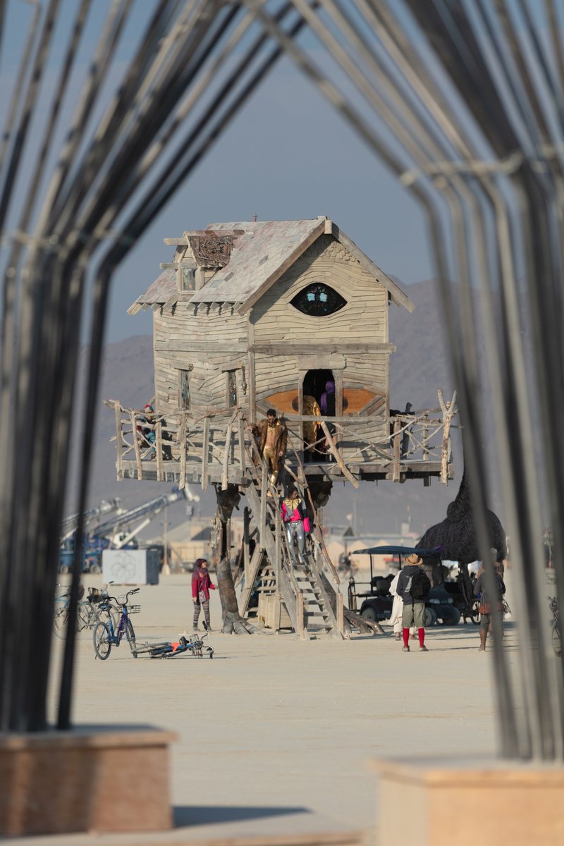 Baba Yaga's House by: Jessi Sprocket Janusee and Baba Yaga's Book Club from: Reno, NV year: 2018 The house of Baba Yaga will rise from the playa straddling it's mechanical chicken legs. The crone's house will be poised to run at the slightest provocation. Ascend her staircases to test the old witch if you dare. Are you able to walk through the veil of mortality into the space where the seer dwells? If you are strong of will, feeling bold and willing to show vulnerability she may allow you to venture within her sanctum. URL: http://jessisprocket.com/baba-yaga/
