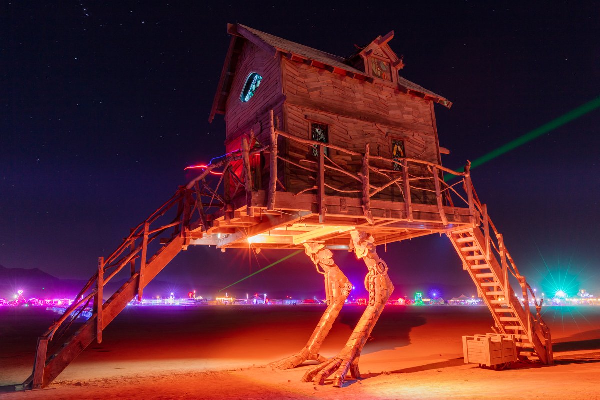 Baba Yaga's House by: Jessi Sprocket Janusee and Baba Yaga's Book Club from: Reno, NV year: 2018 The house of Baba Yaga will rise from the playa straddling it's mechanical chicken legs. The crone's house will be poised to run at the slightest provocation. Ascend her staircases to test the old witch if you dare. Are you able to walk through the veil of mortality into the space where the seer dwells? If you are strong of will, feeling bold and willing to show vulnerability she may allow you to venture within her sanctum. URL: http://jessisprocket.com/baba-yaga/
