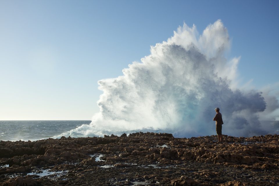 Man And Massive Wave Exploding On Shore