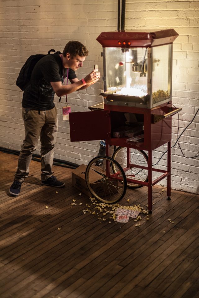 Young Man Taking a Photo With His Cell Phone of a Popcorn Machine XOXO 2013
