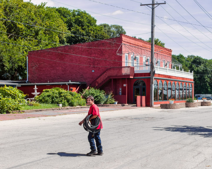 Man with Coiled Hose and Red Building